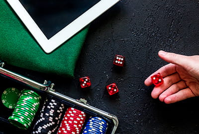 Ein Mann würfelt auf einem schwarzen Tisch, Tablet und Spielchips im Hintergrund.